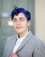 Seated man in suit, tie, and glasses, gesturing with his hands