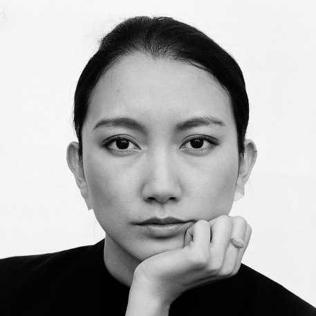Japanese woman cups her chin with one hand and gazes into the camera