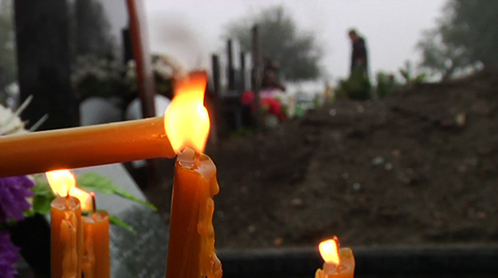 Film still from Letter for Dad. Candle being lit in foreground of graveyard