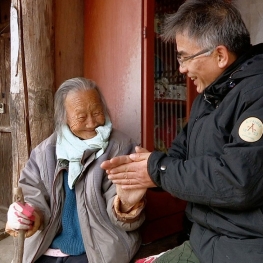 Film still from The Wandering Chef. A man sitting on the right next to an elderly woman to his left in Korea. 