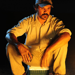 Film still from The Darkside. Man sits in front of campfire outdoors.