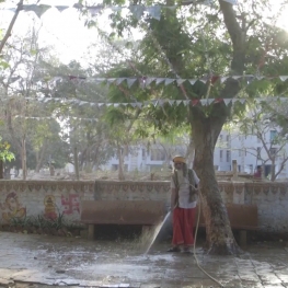 Film still from Welcome Valentine. A Hindu priest in India uses a hose to spray down a court yard. 