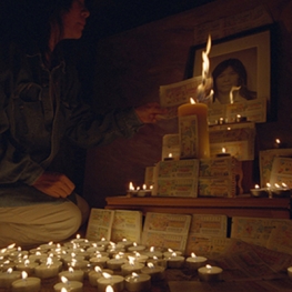 Film still from Ghosts and Numbers. Woman lighting a candle next to a grave.