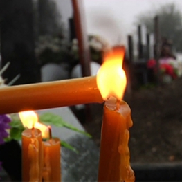 Film still from Letter for Dad. Candle being lit in foreground of graveyard
